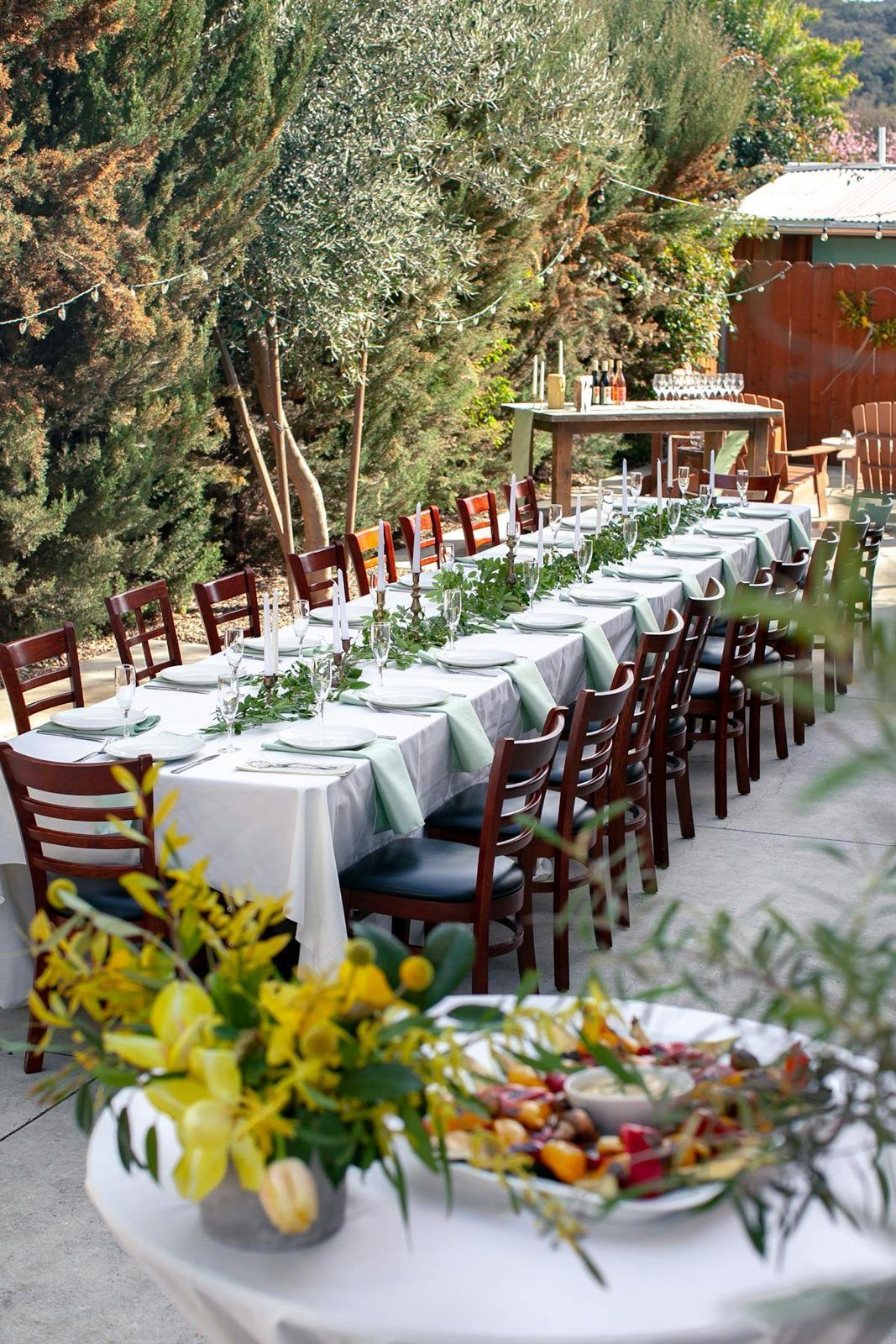 Long banquet table set with white linens and greenery in the courtyard